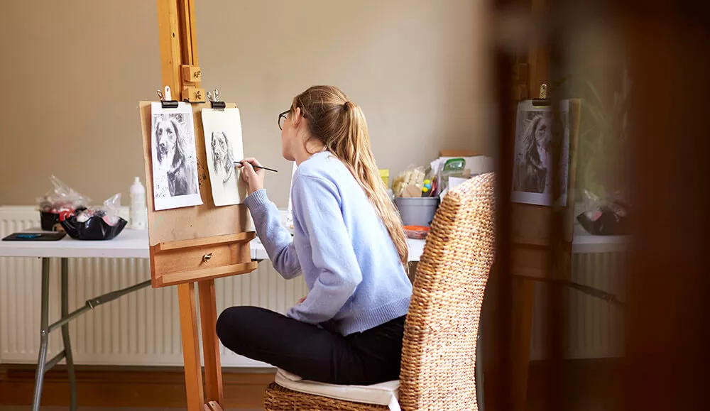 a girl with a ponytail and glasses, drawing a dog from a reference photo