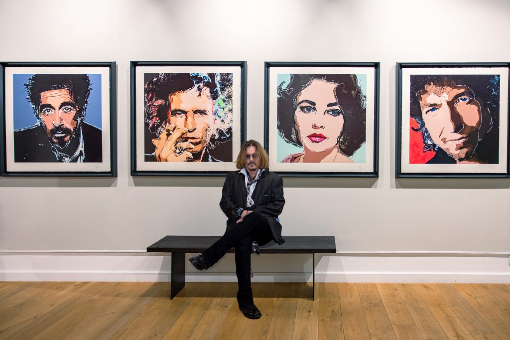 johnny depp standing in front of a wall with 4 of his paintings behind him